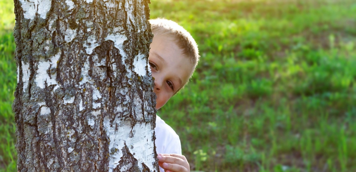 Junge schaut schüchtern hinter einem Baum hervor 