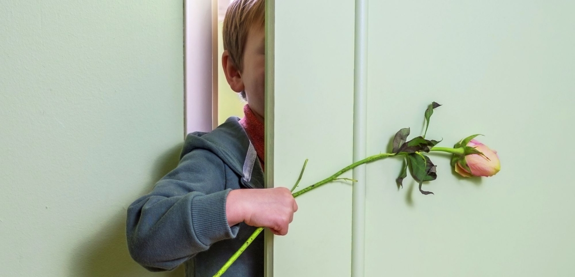 Kind mit Rose in der Hand spitzt durch halb geöffnete Zimmertür 