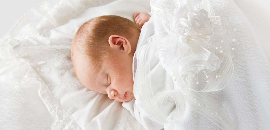Schlafendes Baby im weißen Kleid liegt auf weißem Kissen