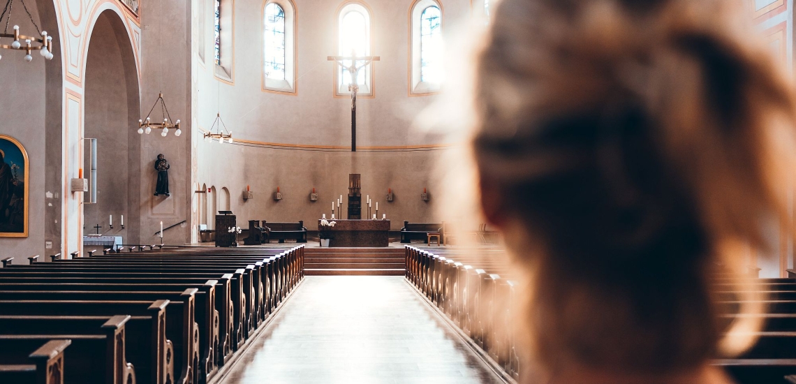 Frau blickt von hinten in einen leeren Kirchenraum