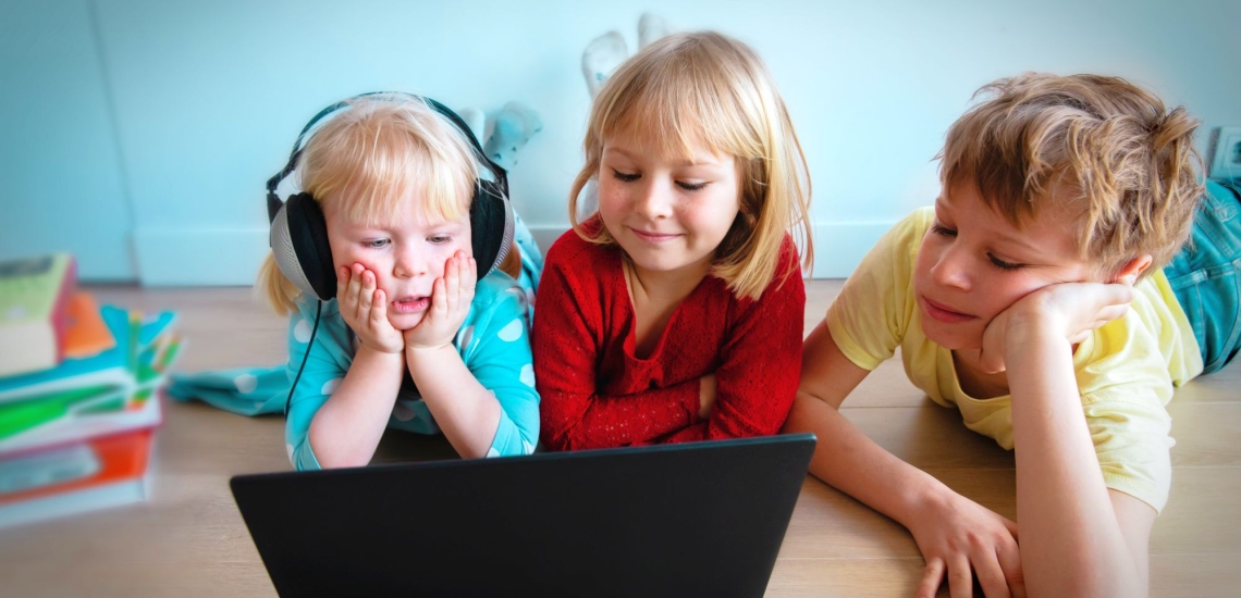 drei Kinder liegen auf Boden und schauen auf Notebook 