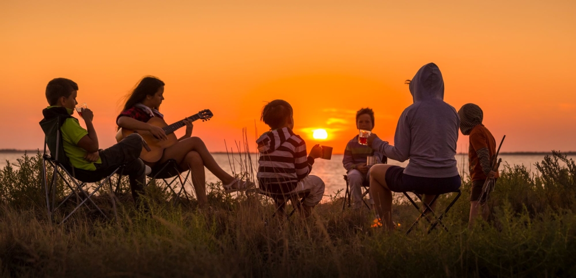 Kinder und Jugendliche im Kreis mit Gitarre im Sonnenuntergang