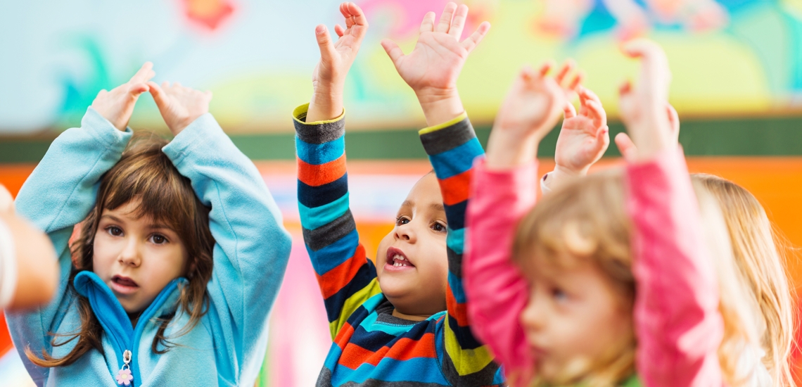 Drei Kinder halten ihre Arme nach oben und machen Bewegungen zu einem Lied nach.