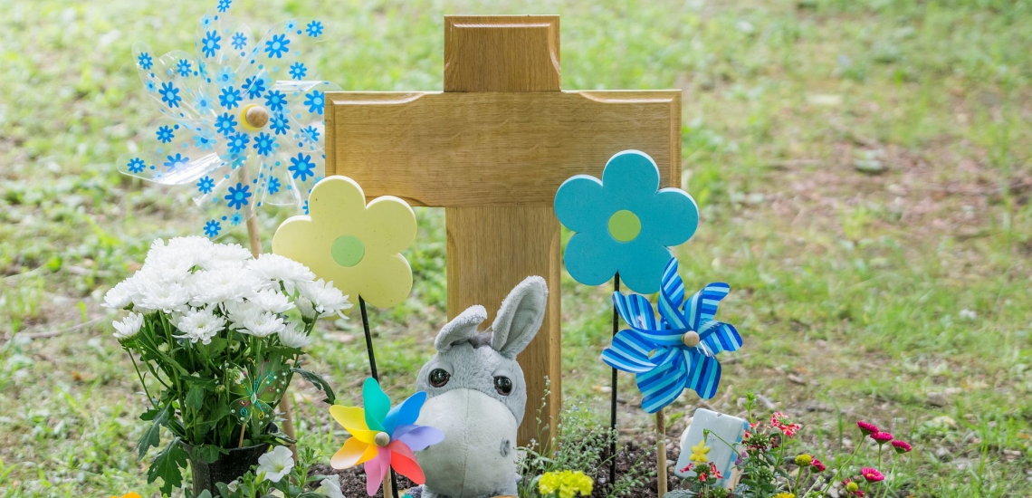 Kindergrab mit Kreuz, Kuscheltieren und bunten Windrädern