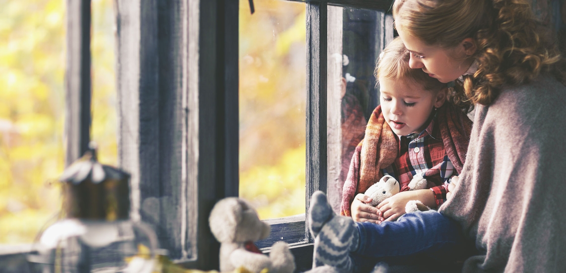 Eine Mutter sitzt mit ihrem Kind am Fenster, sie kuscheln sich aneinander.