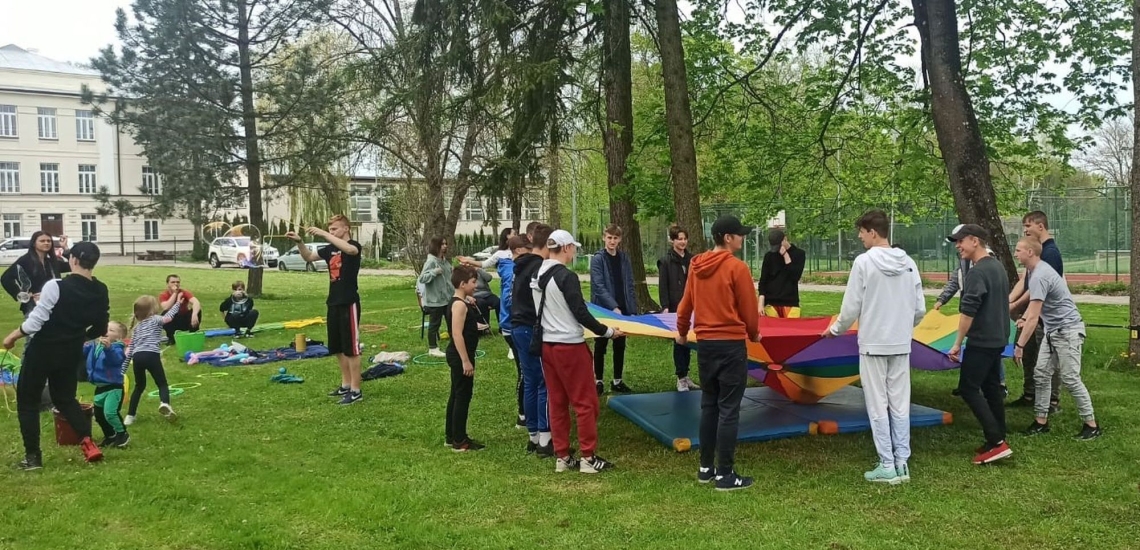 Kinder und Jugendliche spielen in Park mit buntem Tuch 