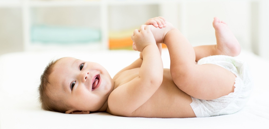 Baby liegt lachend im Bett und spielt mit seinen Füßchen 