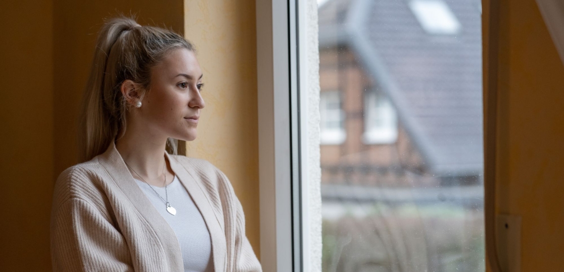 Jugendliche steht am Fenster und schaut nach draußen