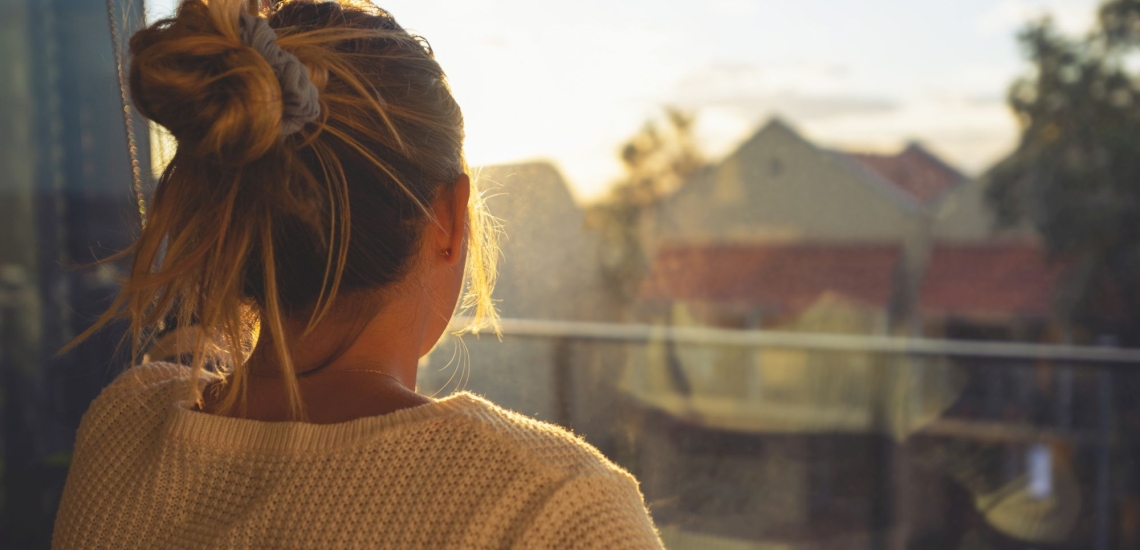 Frau von hinten schaut aus Fenster 