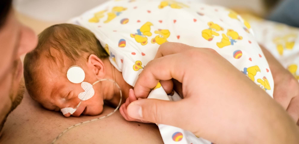 Ein Papa hält sein Frühchen mit Schlauch in der Nase auf seiner nackten Brust.