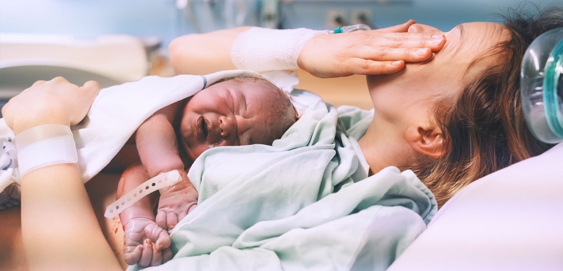Mutter erschöpft nach der Geburt hält sich Hand über die Augen mit Baby auf dem Bauch 