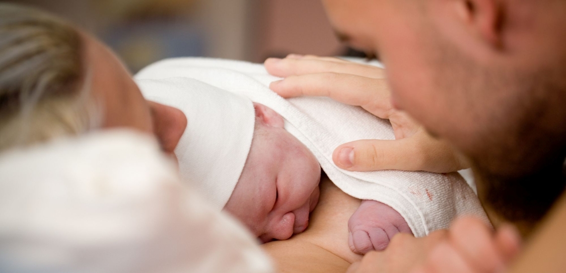 Nach der Geburt liegt Baby auf Bauch von Mutter Vater streichelt es