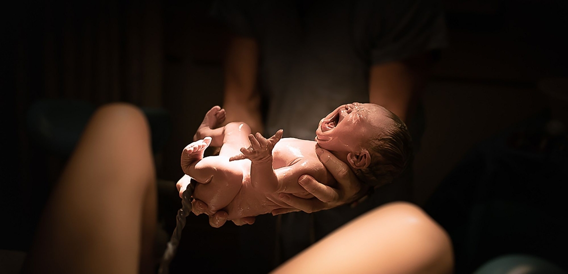 Geburt neugeborenes Kind mit Nabelschnur wird über Bauch von Mutter gehalten