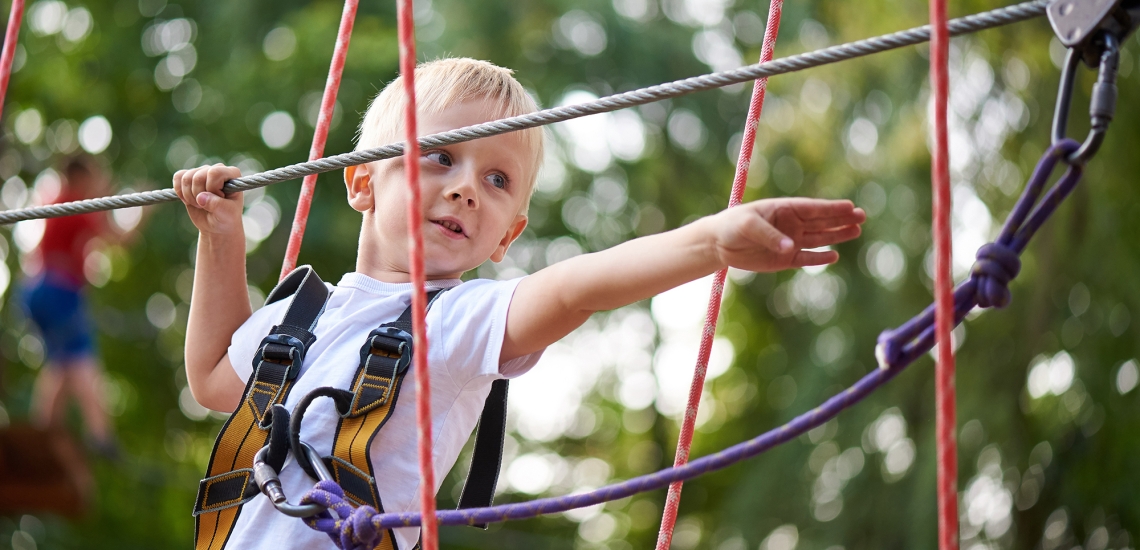 Ein Junge hangelt sich im Kletterparcours von Seil zu Seil.
