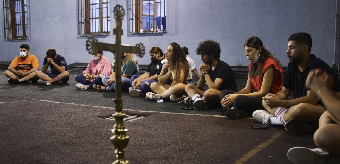 Junge Männer und Frauen sitzen im Kreis um ein Kreuz und beten 