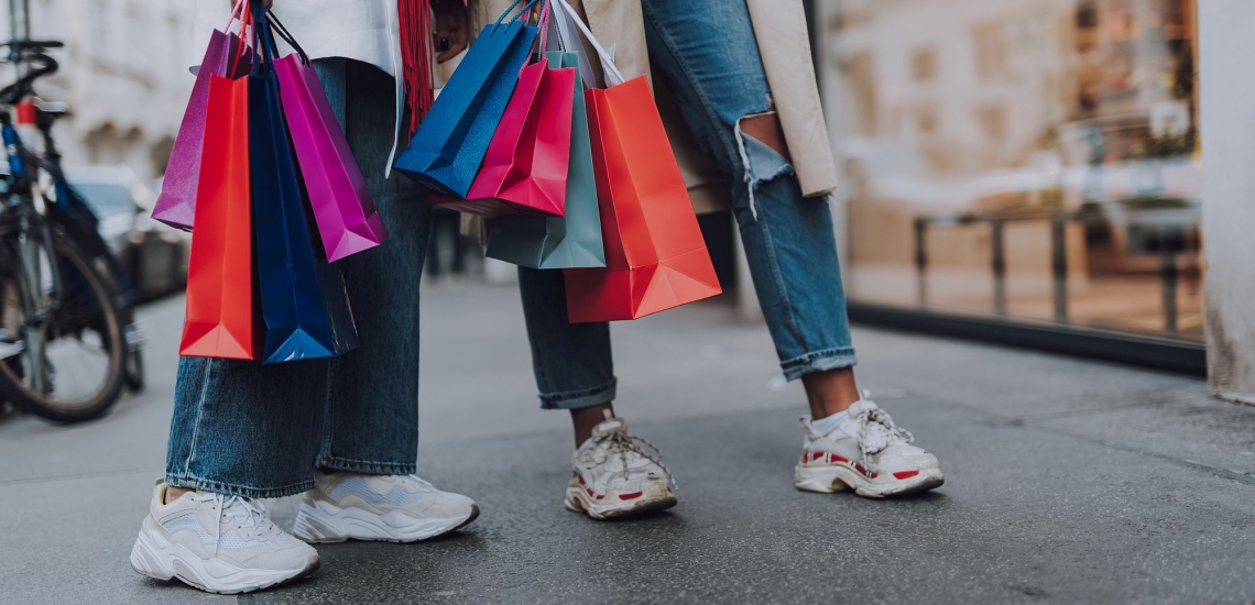 Beine von zwei jungen Frauen in Jeans und Turnschuhen mit vielen Einkaufstaschen 