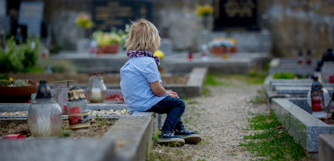 Kind sitzt auf Grab auf einem Friedhof 