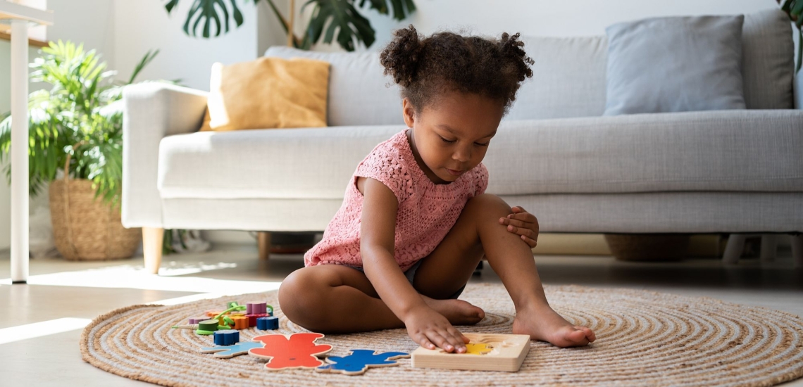 Mädchen spielt mit Holzspielzeug auf Wohnzimmerteppich