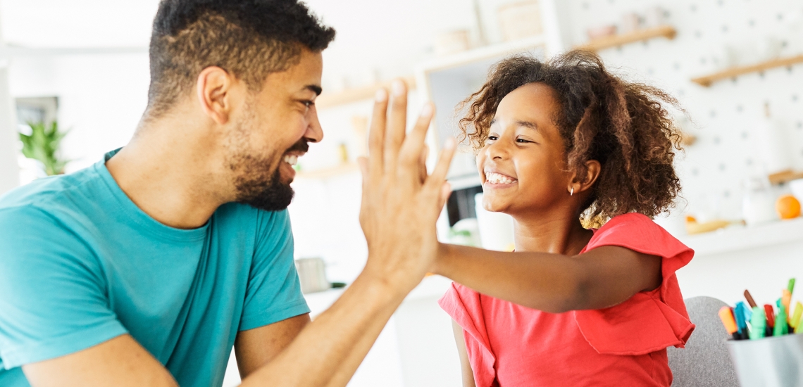 High five zwischen einem Mädchen und ihrem Vater, beide lachen dabei.