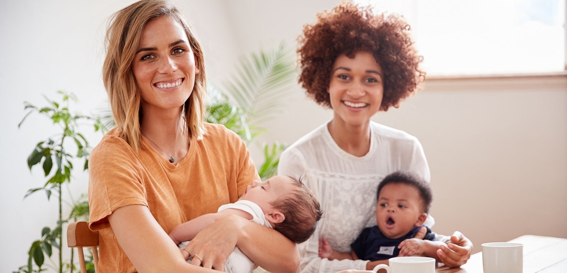 zwei Mütter halten ihre Babies im Arm und trinken Kaffee 