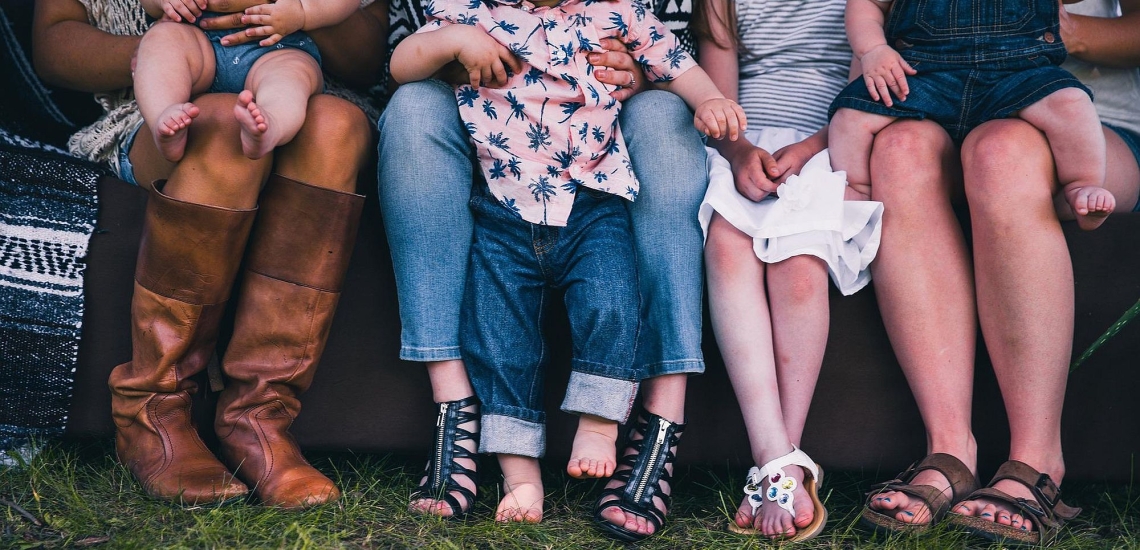 Beine und Schuhe von Müttern, die auf einer Bank sitzen und ihre Kinder auf dem Schoß haben 