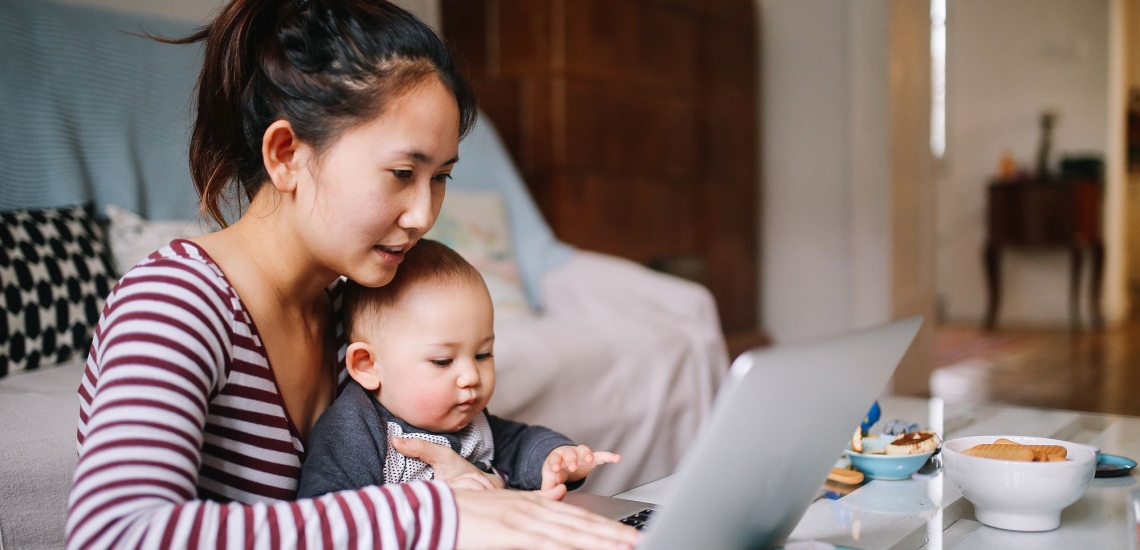 Mutter am Laptop zuhause mit Baby auf dem Schoß