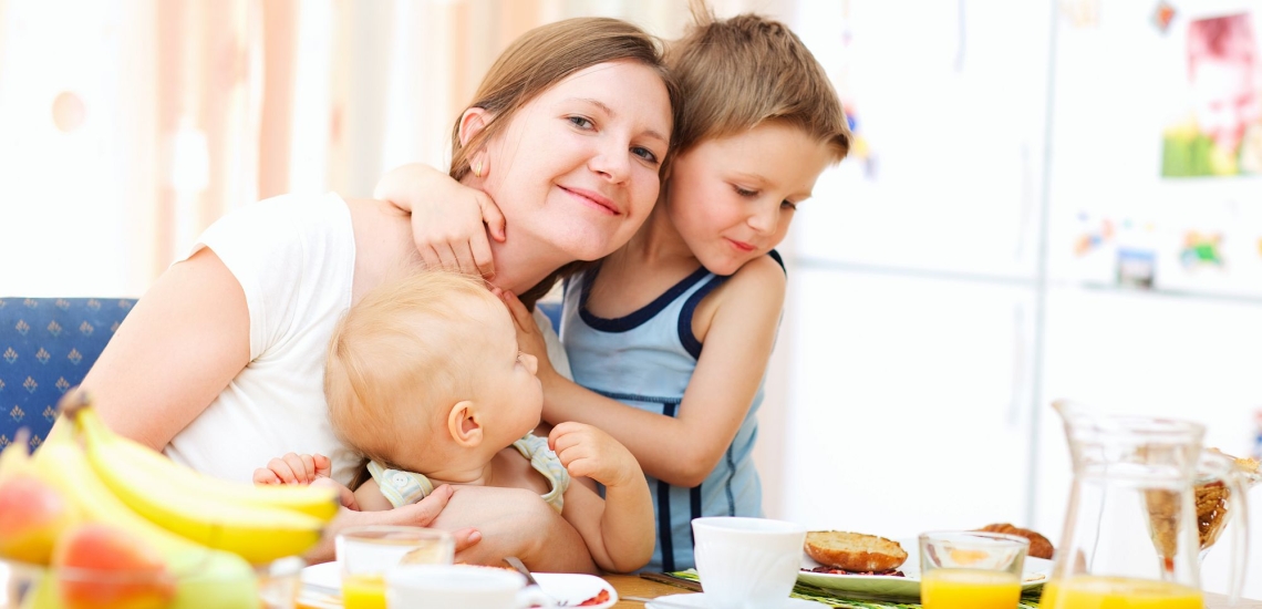 Mutter lachend mit zwei Kindern am Esstisch 