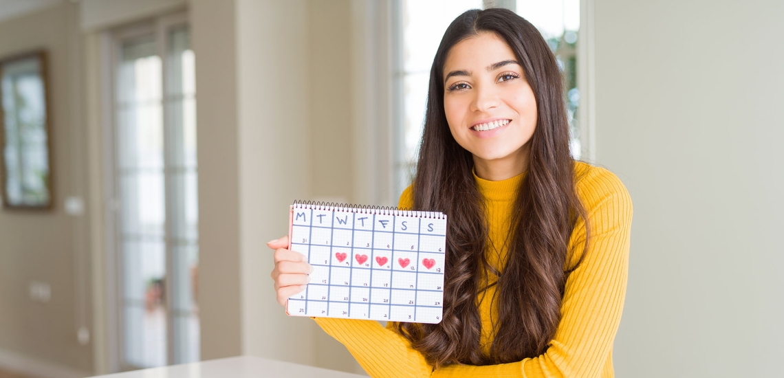 Ein junges Mädchen hält lächelnd ein Kalender in ihrer Hand, in dem ihre Tage eingezeichnet sind.