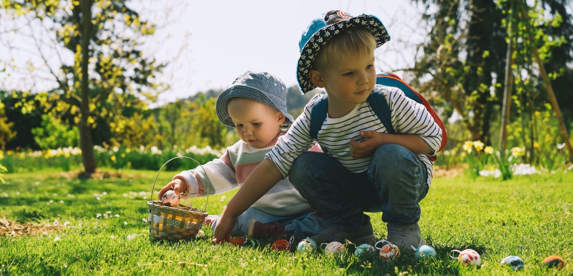 zwei Kinder suchen Ostereier auf Wiese