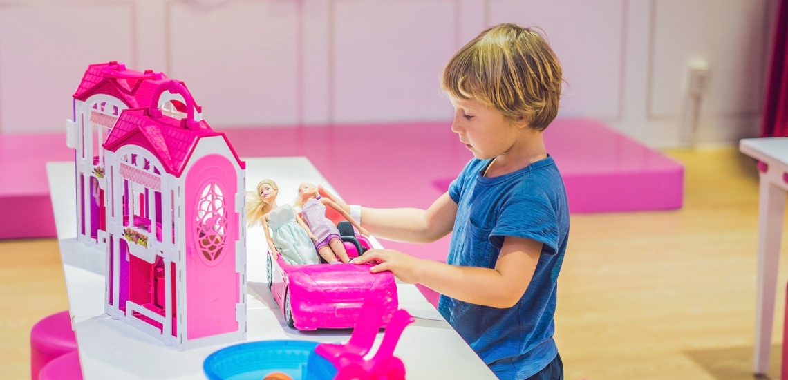 Ein Junge spielt mit einem pinken Barbiehaus und Barbiepuppen.