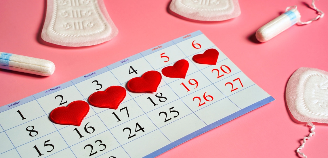 Auf einem Wochenkalender sind rote Herzchen verteilt. Daneben liegen Binden und Tampons.