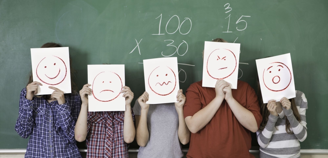 Schulkinder halten sich Blätter mit Smileys vors Gesicht