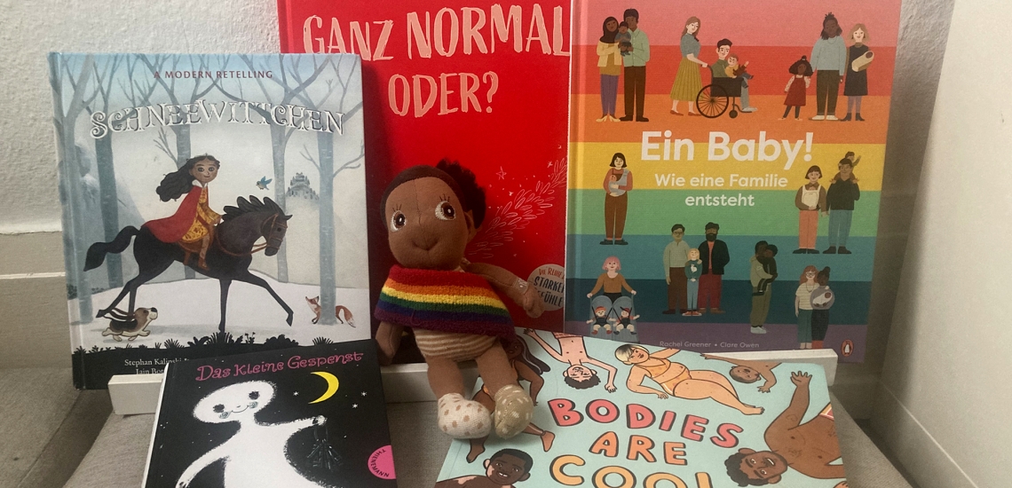 Queere Kinderbücher und eine Puppe of Colour lehnen an einer Wand.