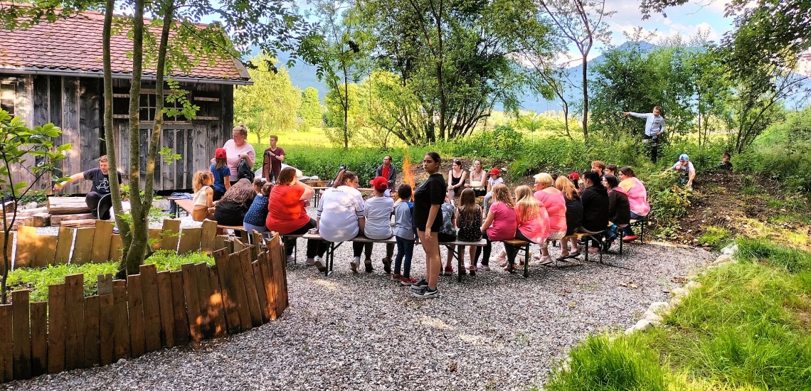 Eltern und Kinder sitzen im Kreis im Grünen bei einer Veranstaltung des Aktionszentrums Benediktbeuern 