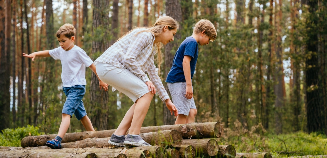 Kinder balancieren im Wald auf am Boden liegenden Holzstämmen 