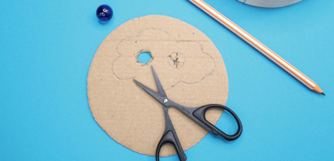 bemalter Boden von Pappschachtel mit Schere, Stift und ausgeschnittenem Loch