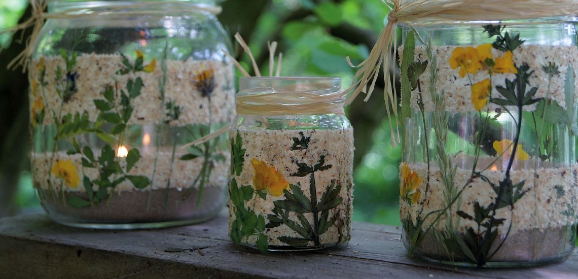 drei mit Sand gefüllte Gläser mit Blumen und Kerzen