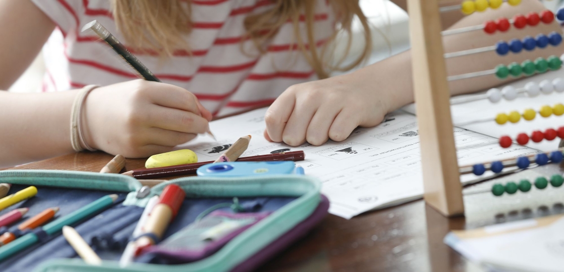 Hände von Kind beim Hausaufgabenmachen mit Heften und Federmäppchen 