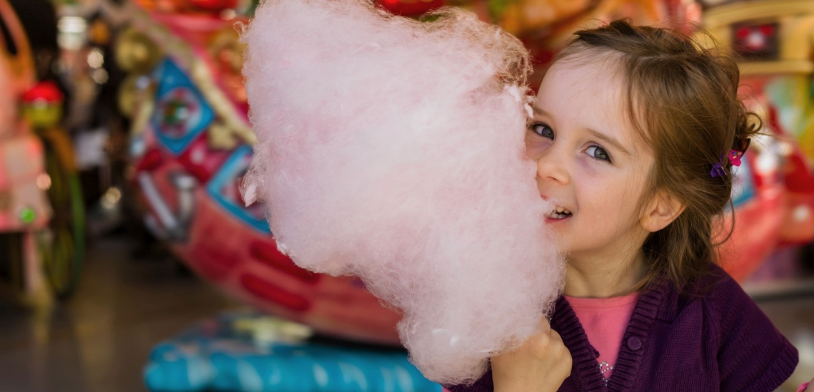 Mädchen mit Zuckerwatte vor Verkaufsstand auf Fest 