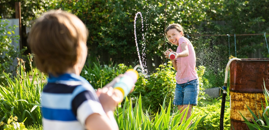 zwei Kinder spritzen sich im Garten mit Wasserspritzen nass 