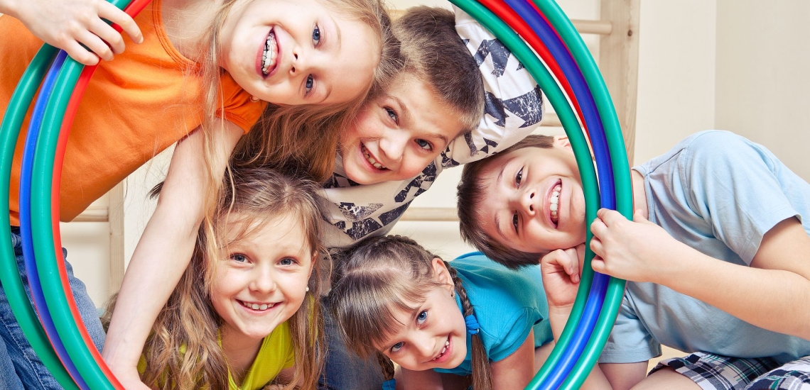 Kinder in Turnhalle schauen glücklich durch Hullahoop-Reifen 