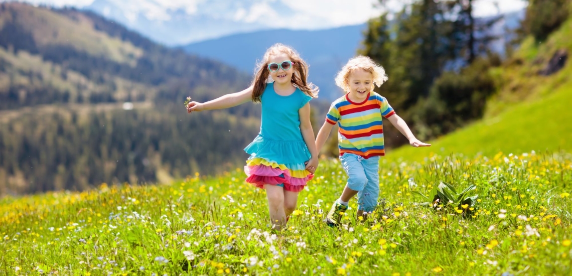 Mädchen und Junge laufen glücklich über Bergwiese im Sommer 