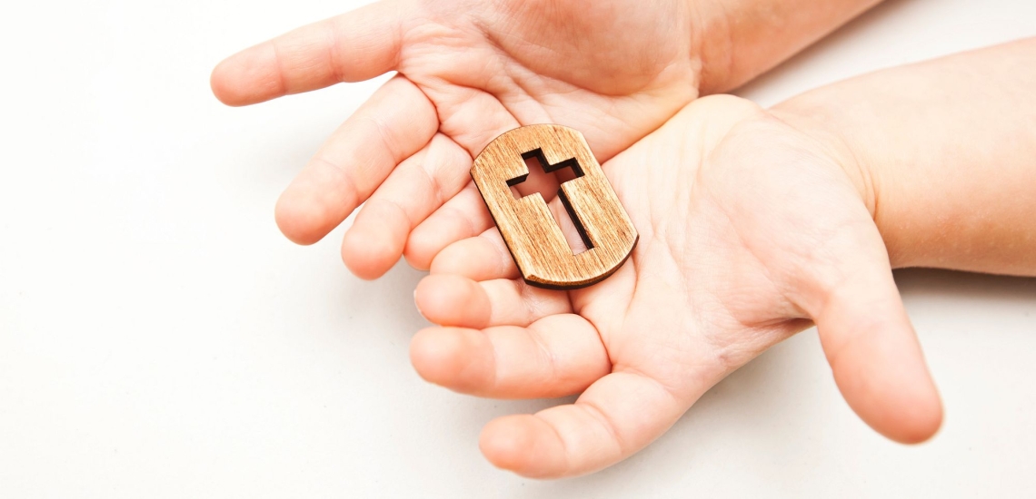 Kinderhände halten kleines Kreuz aus Holz 
