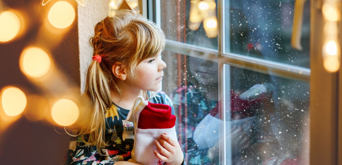 Mädchen sitzt nachdenklich an Fenster mit Weihnachtsbeleuchtung