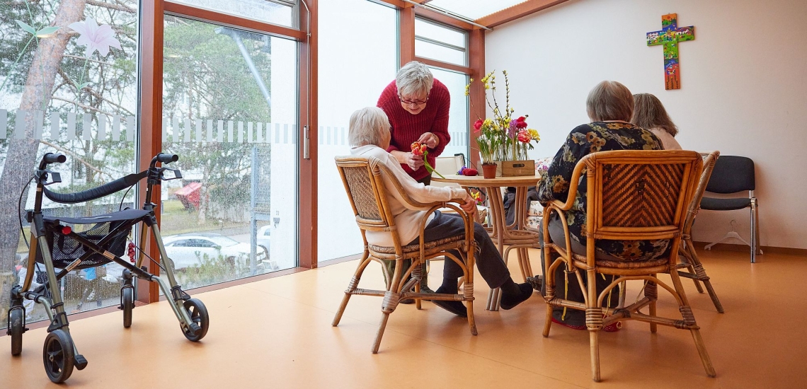 Seniorinnen sitzen um Tisch und lassen sich von Gartentherapeutin Bärbel Zirker die Blumen zeigen 