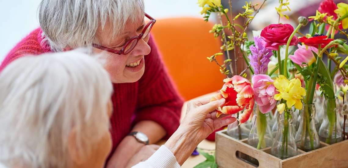 Seniorin und Gartentherapeutin Bärbel Zirker betrachten mitgebrachte bunte Blumen 