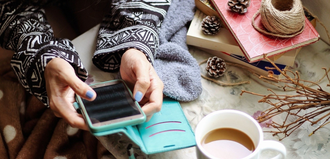 Frau macht es sich gemütlich mit Smartphone, Büchern und einer Tasse Kaffe