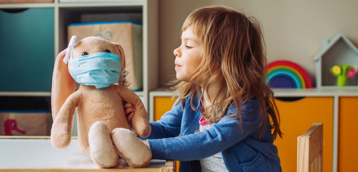 Kindergartenkind mit Stoffhase, der Mund-Nasen-Maske trägt 