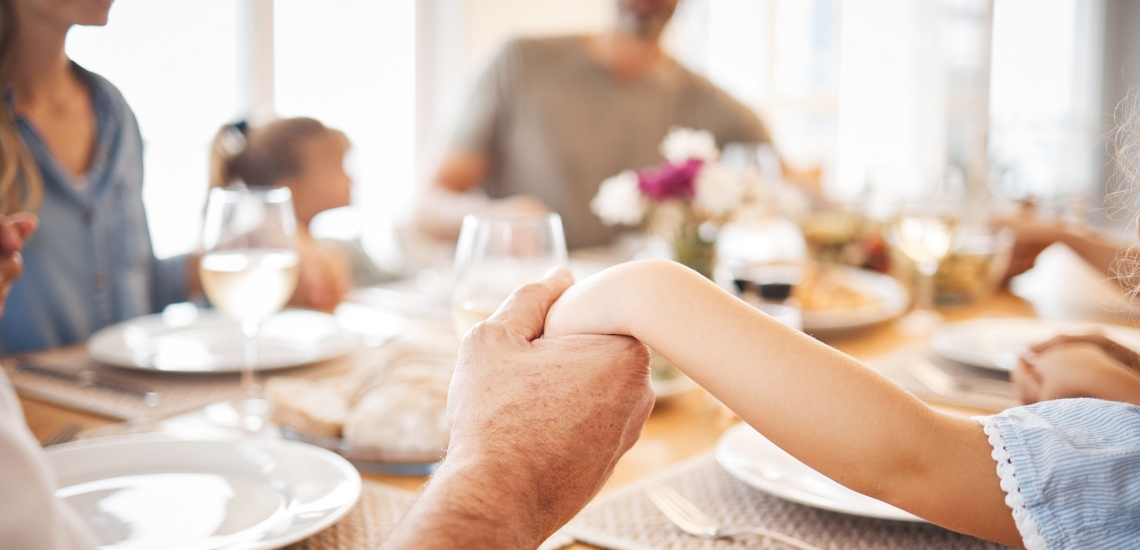 Menschen geben sich die Hände bei Tischgebet mit Familie vor dem Essen 