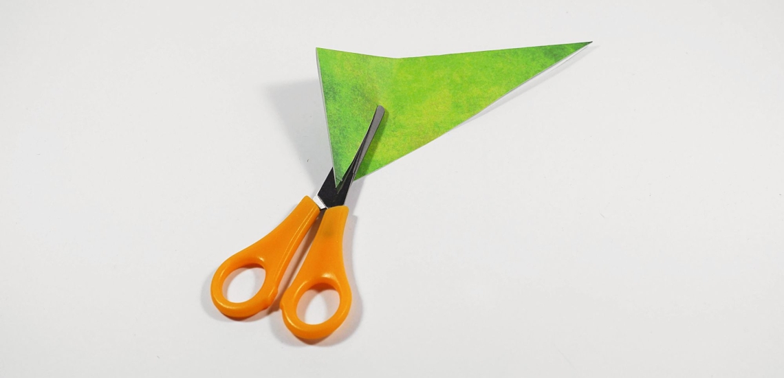 Schere schneidet in grünes Papierdreieck